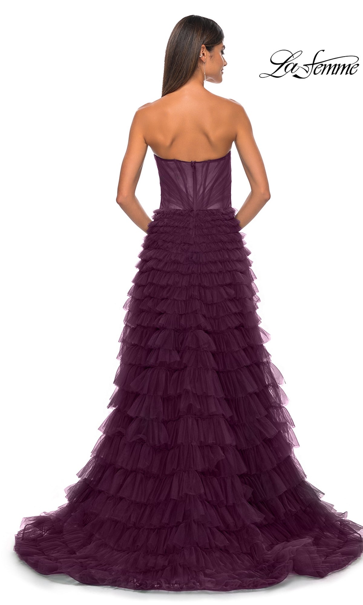 A woman stands with her back to the camera in the La Femme Strapless Long Ruffled Prom Dress 32283, a floor-length deep purple gown with layered ruffles. The La Femme logo appears in the top right corner.